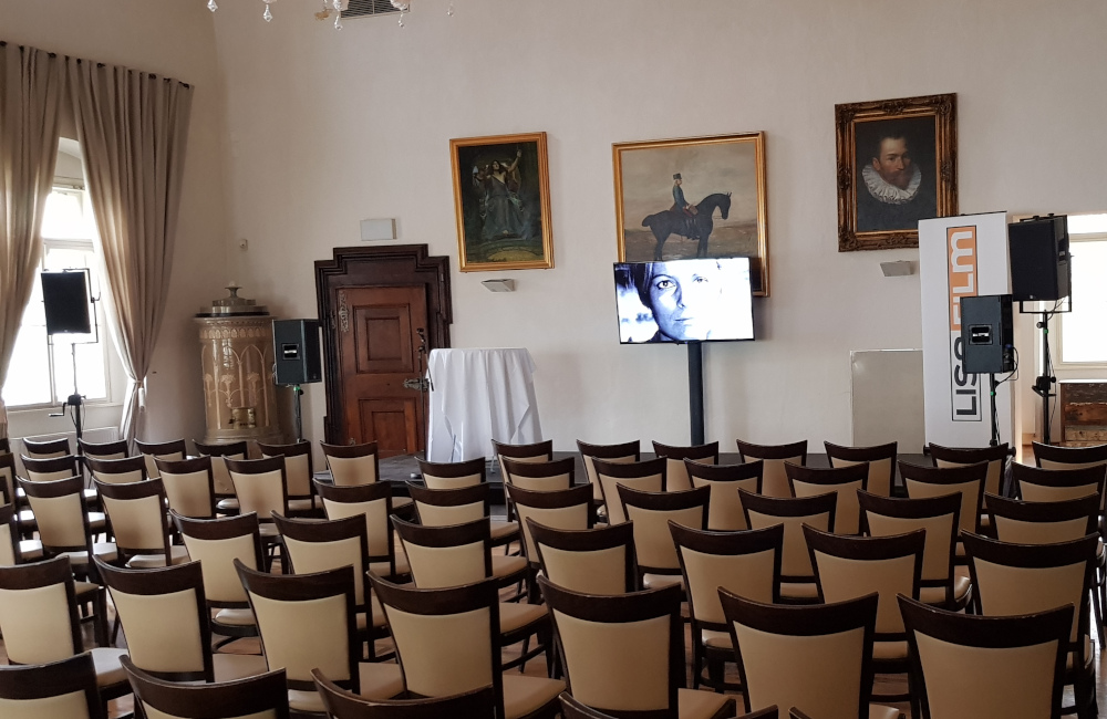 Vortragssaal mit Bühne, Flat-TV auf SMS Stativ und Meyer Sound Lautsprechern auf Stativen in Klagenfurt Schloss Maria Loretto