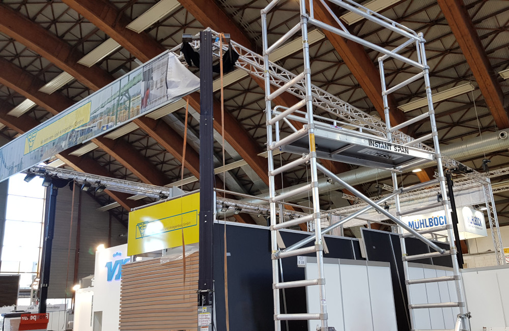 Rudnick & Enners Messestand Aufbau der Traversen, Banner und HQI Beleuchtung auf der Messe Holzbau in Klagenfurt